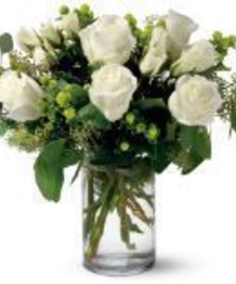 White roses and green berries in a glass cylinder vase.