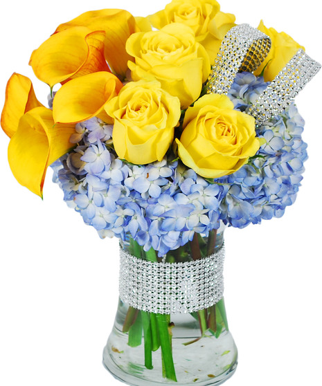 Sunset callas, yellow roses and blue hydrangea in a clear glass vase with a touch of bling.