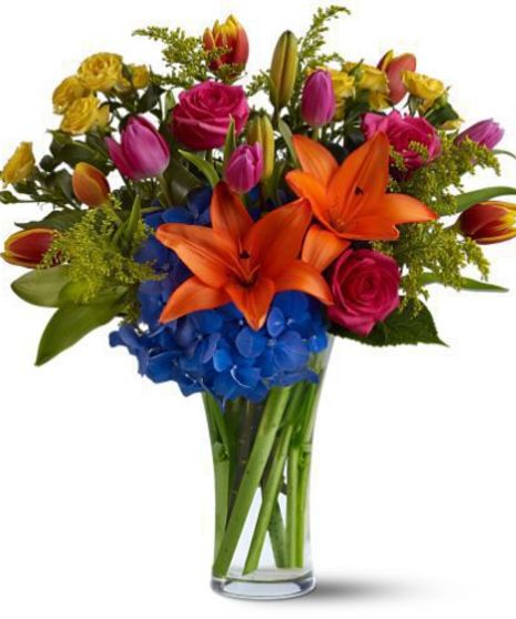 Bright orange, blue and pink flowers in a clear glass vase.