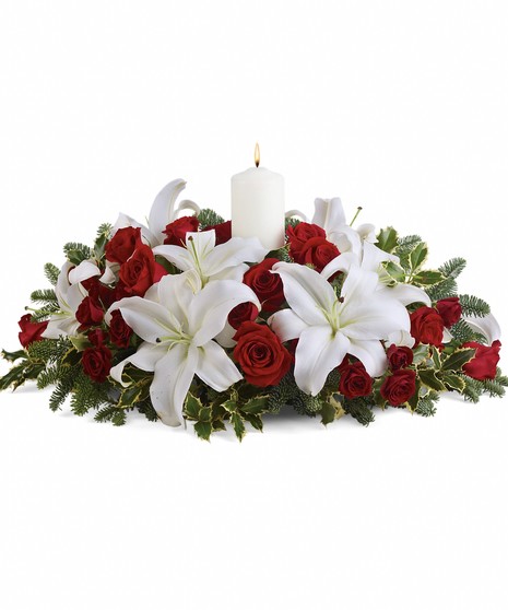 A dozen red roses, white Asiatic lilies and fresh evergreens are arranged in a dish around a white pillar candle