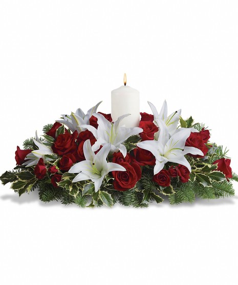A dozen red roses, white Asiatic lilies and fresh evergreens are arranged in a dish around a white pillar candle
