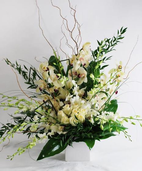 All-white arrangement of orchids and roses in a white cube vase with greenery.