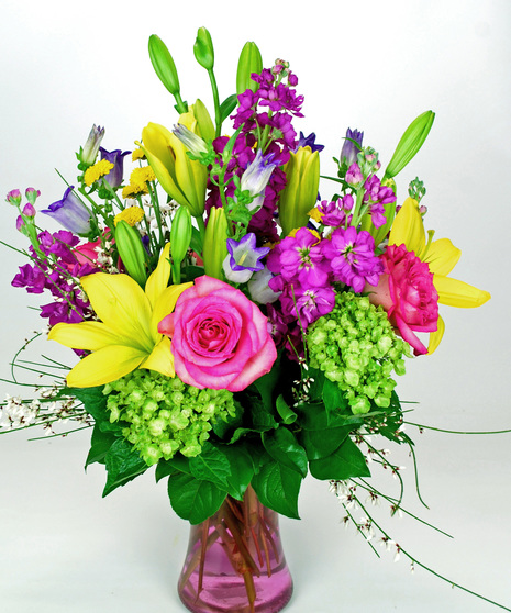 Stock, lily, roses, and hydrangea in a clear pink glass vase.