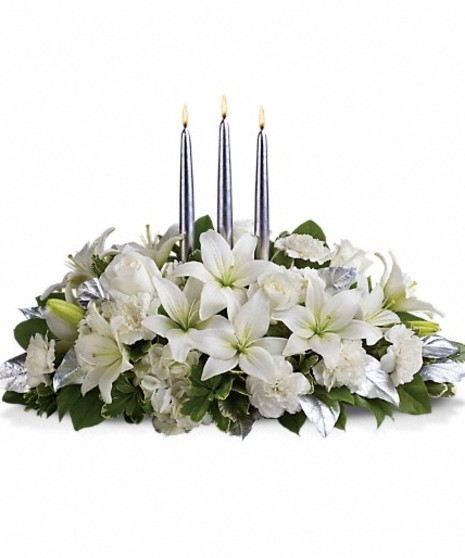 Winter centerpiece of white hydrangea, roses, asiatic lilies, carnations and greenery with three silver taper candles.