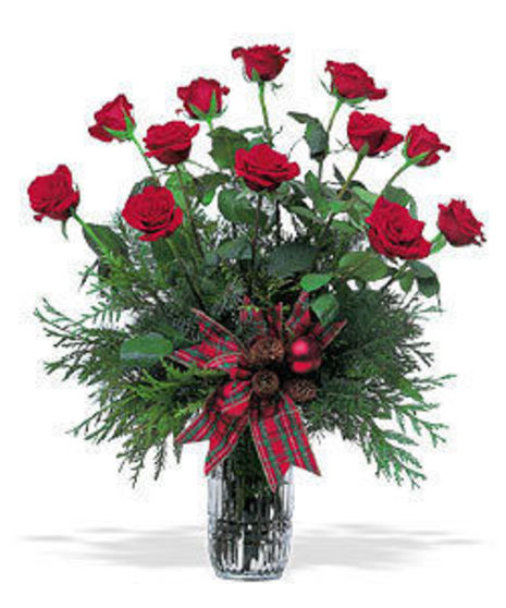 Red roses and winter greenery in a glass vase tied with ribbon. 