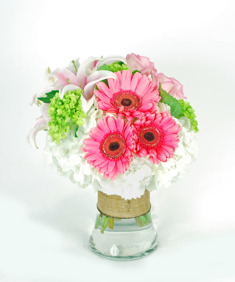 Pink oriental lilies, green hydrangea, pink gerbera daisies, and roses in a clear glass vase.