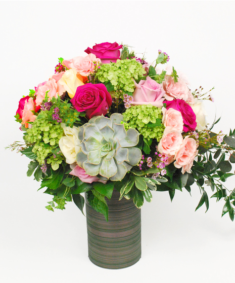 Lime green hydrangeas, hot pink and white roses, light pink spray roses, wax flower, and assorted greens with a succulent.
