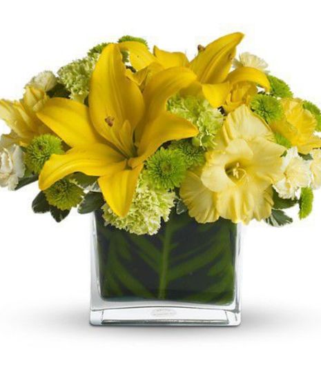 Yellow lilies and green flowers in a glass cube vase.