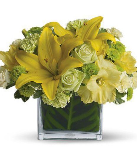 Yellow lilies and green flowers in a glass cube vase.