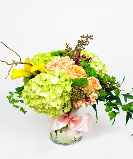 Lime green hydrangea, yellow callas, peach roses and purple was flower in a clear glass vase tied with a bow.