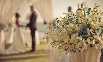 A blurry image of a couple holding hands in front of a bouquet of white wedding flowers.